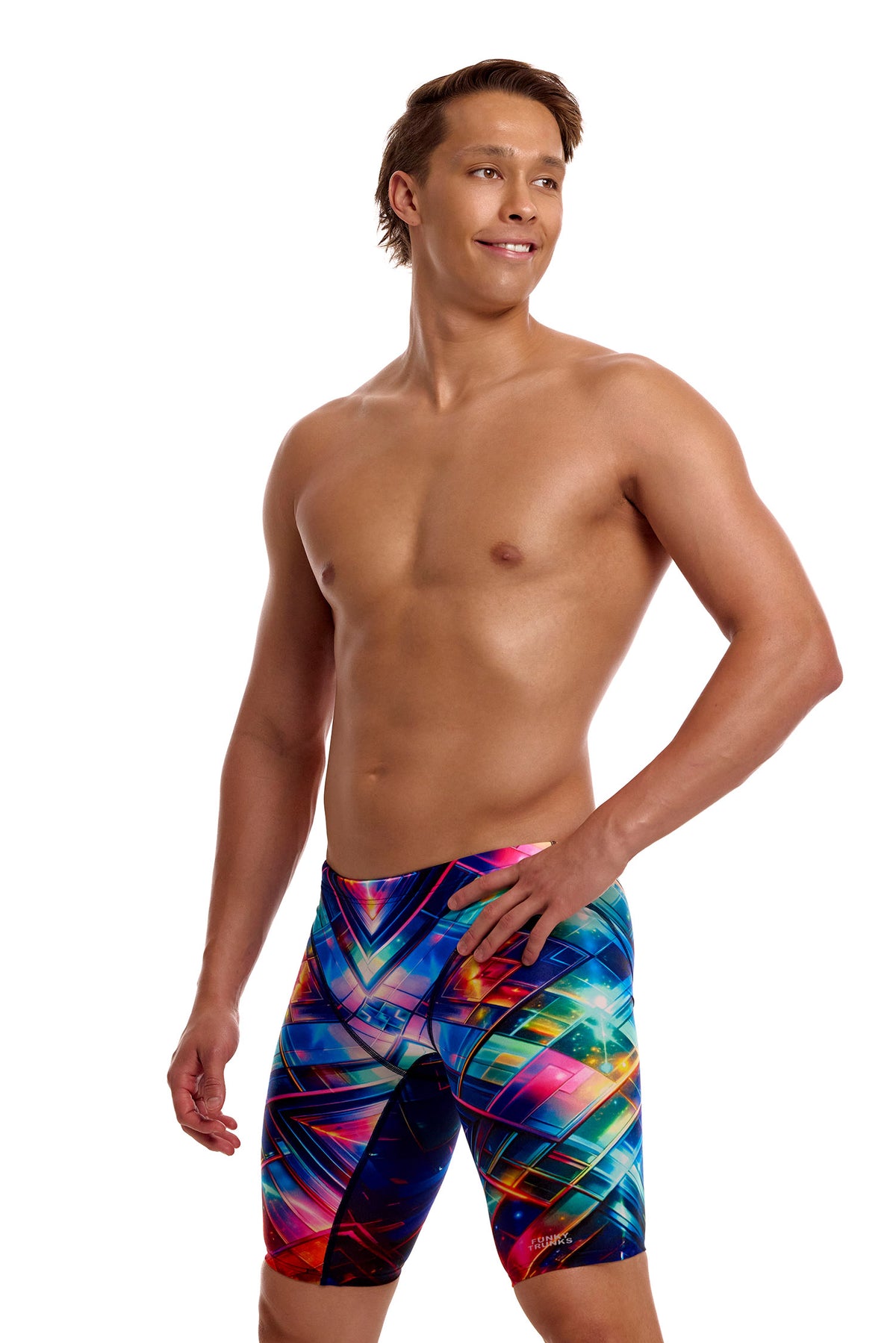 A male athlete standing against a solid white background modeling the Funky Trunks "Firefly Sparkle" Men's Fast Training Jammers, featuring a multi-colored geometric pattern across the swim jammers.