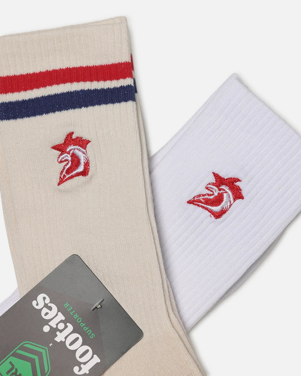 Two pairs of crew socks displayed diagonally on a light gray background. One pair is cream/beige with red and navy blue stripes near the cuff and a red and white bird logo embroidered on the front.