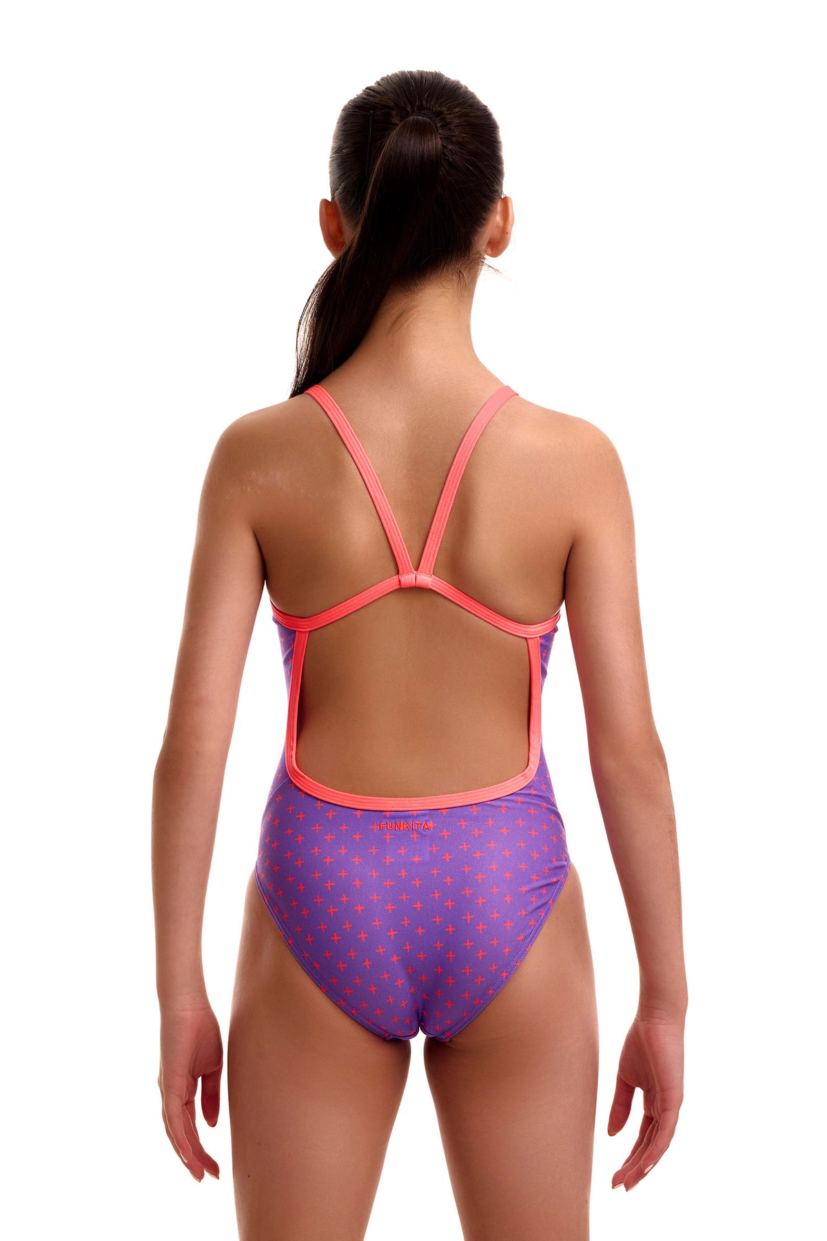 Back view of a young girl wearing the Funkita Single Strap swimsuit in purple with an orange plus/cross pattern, showing thin peach single-bind straps, an open back cutout, and the orange 'FUNKITA' logo across the lower back.