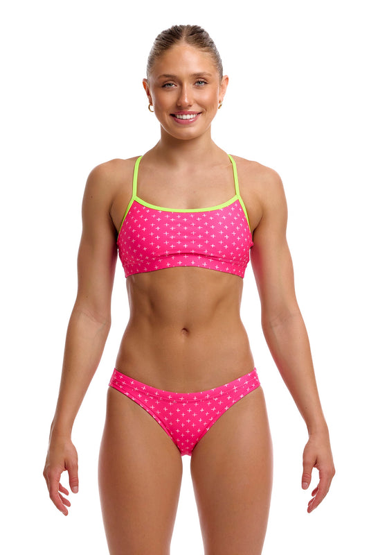 A female model standing against a white background wearing the Funkita "Pink Proton" Women's Swim Crop Top and matching bottoms, featuring a vibrant pink pattern accented with bright lime green thin shoulder straps.