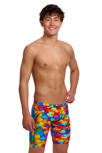 A young male model standing against a white background wearing the Funky Trunks "Try The Lot" Boys Training Jammers, featuring a bright, multi-colored geometric pattern with red, yellow, blue, and green