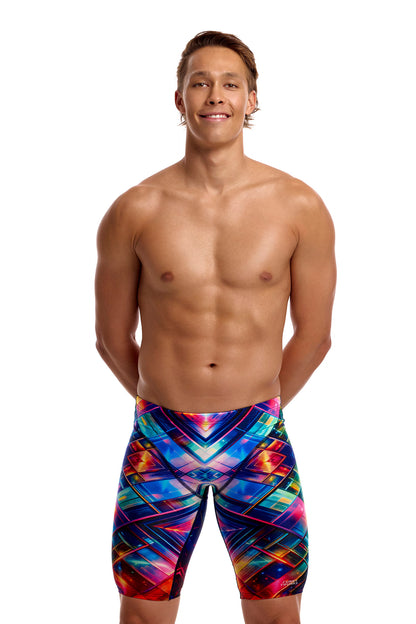 A male athlete standing against a solid white background modeling the Funky Trunks "Firefly Sparkle" Men's Fast Training Jammers, featuring a multi-colored geometric pattern across the swim jammers.