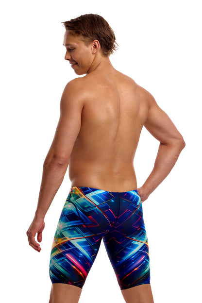 A male athlete standing against a solid white background modeling the Funky Trunks "Firefly Sparkle" Men's Fast Training Jammers, featuring a multi-colored geometric pattern across the swim jammers.