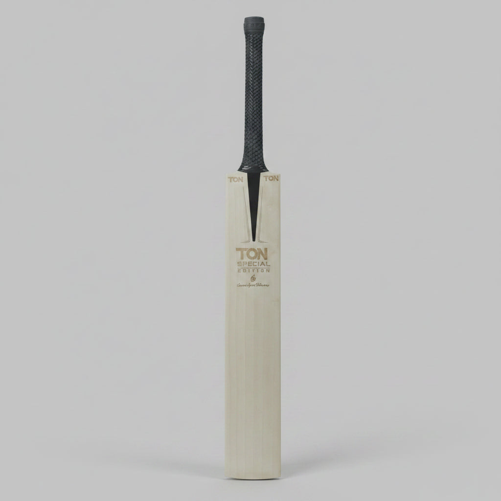 A single cricket bat standing upright against a dark gray background. The bat has a light natural wood blade with gold-toned 'TON' branding and a dark gray textured grip.