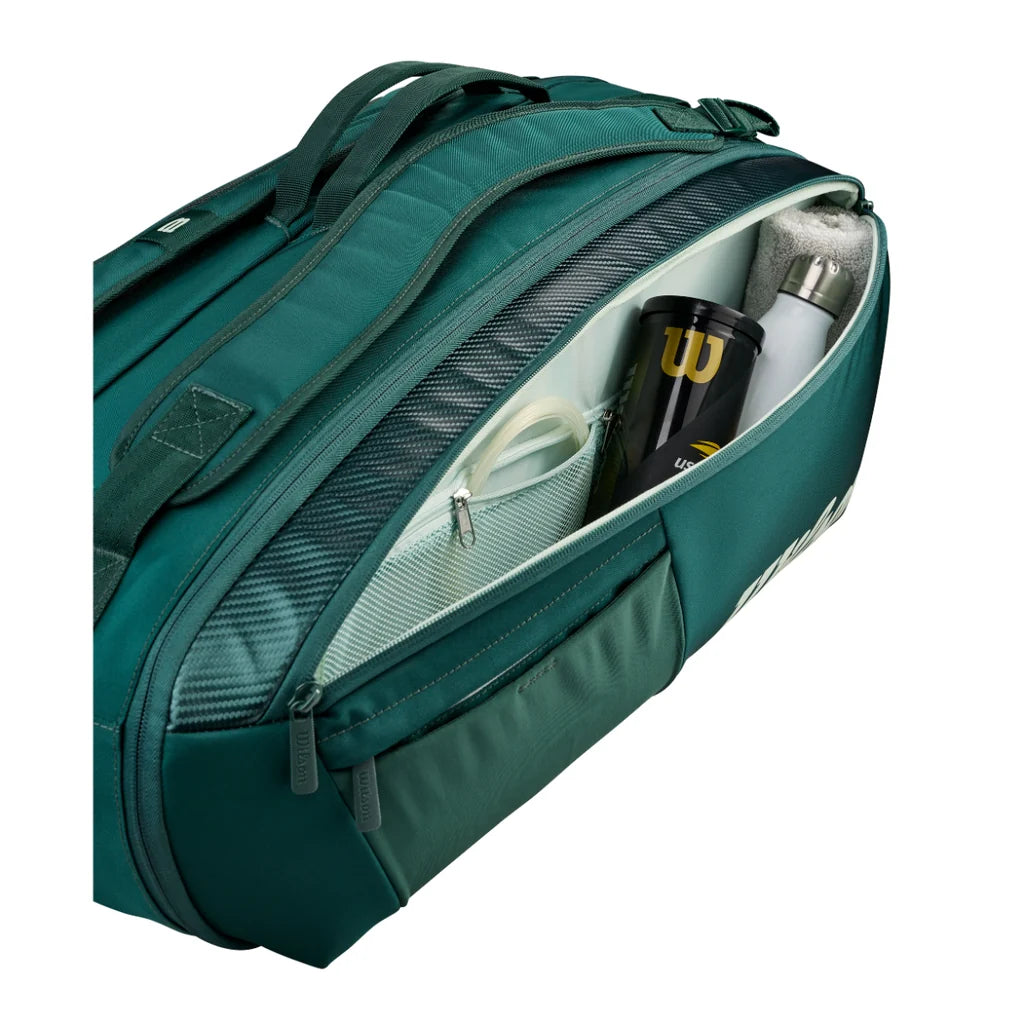 Open accessory compartment of green Wilson Blade V10 bag holding a tennis ball tube, bottle and towel.