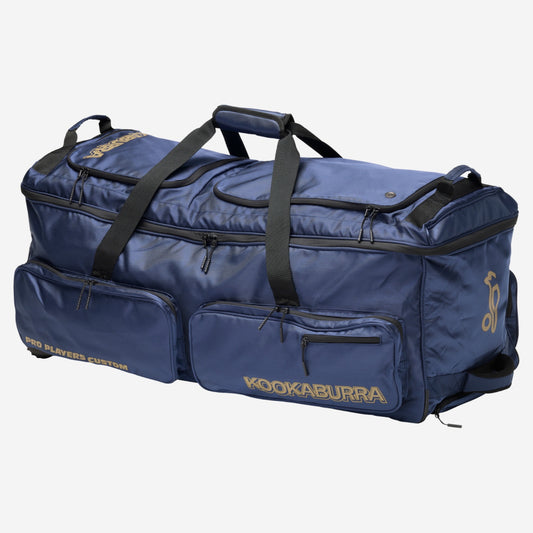 Kookaburra Pro Player Custom Wheel Bag Navy - Angled view showing multiple external pockets, top handles, and tank wheels with gold branding