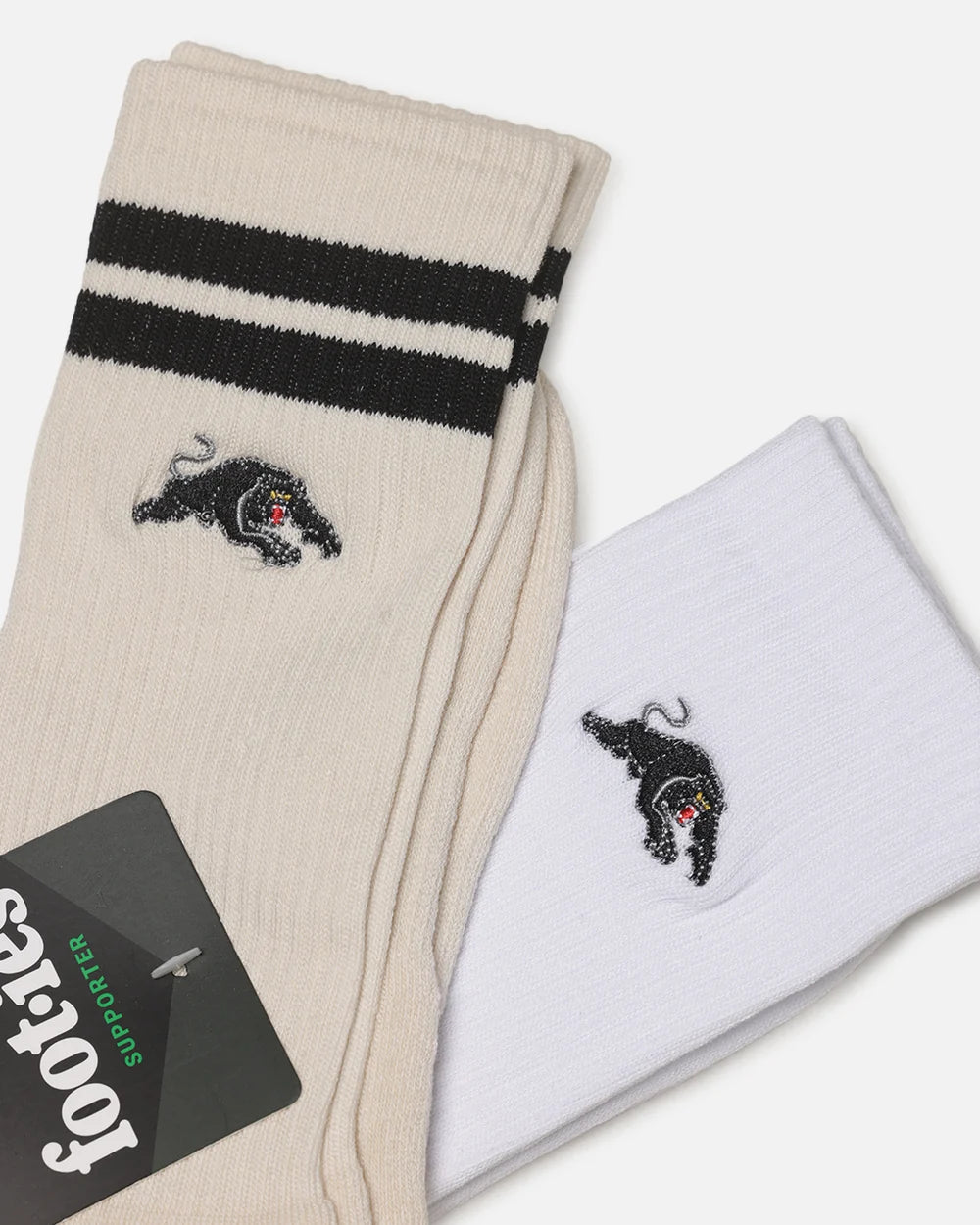 Two pairs of Footes crew socks, one cream and one white, both featuring black stripes near the cuff and a black embroidered panther logo with a small red accent.