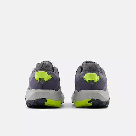 Rear view of grey and black New Balance Big Kids Nitrel Lace trail running shoes, showing the heels with bright yellow pull tabs and yellow accents on the patterned outsoles against a light grey background.