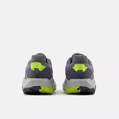 Rear view of grey and black New Balance Big Kids Nitrel Lace trail running shoes, showing the heels with bright yellow pull tabs and yellow accents on the patterned outsoles against a light grey background.