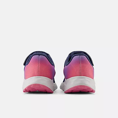 Rear view of New Balance Kids Arishi v4 Hook & Loop running shoes in vintage indigo blue, showcasing gradient pink heels, white Fresh Foam midsoles, and pink outsoles against a light grey background.