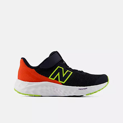 Side profile view of a single black and orange New Balance Kids Arishi v4 Hook & Loop running shoe, showing the dark mesh upper, bright orange heel, white Fresh Foam midsole, and neon green outsole against a light grey background.