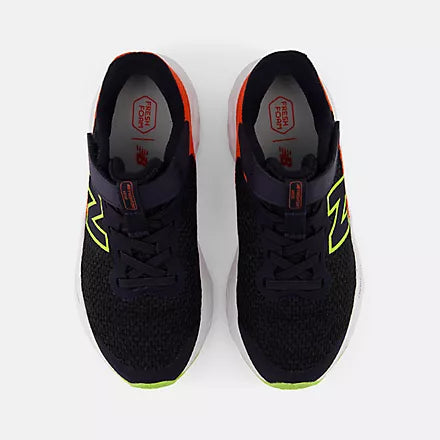 Top view of black New Balance Kids Arishi v4 running shoes placed side-by-side, showing orange collar lining, red Fresh Foam insoles, and bright yellow-green outsoles against a light grey background.