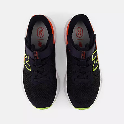 Top view of black New Balance Kids Arishi v4 running shoes placed side-by-side, showing orange collar lining, red Fresh Foam insoles, and bright yellow-green outsoles against a light grey background.