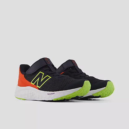 Side view of black and orange New Balance Kids Arishi v4 Hook & Loop running shoes featuring bright green soles, a black mesh upper, and a silver 'N' logo, set against a light grey background.